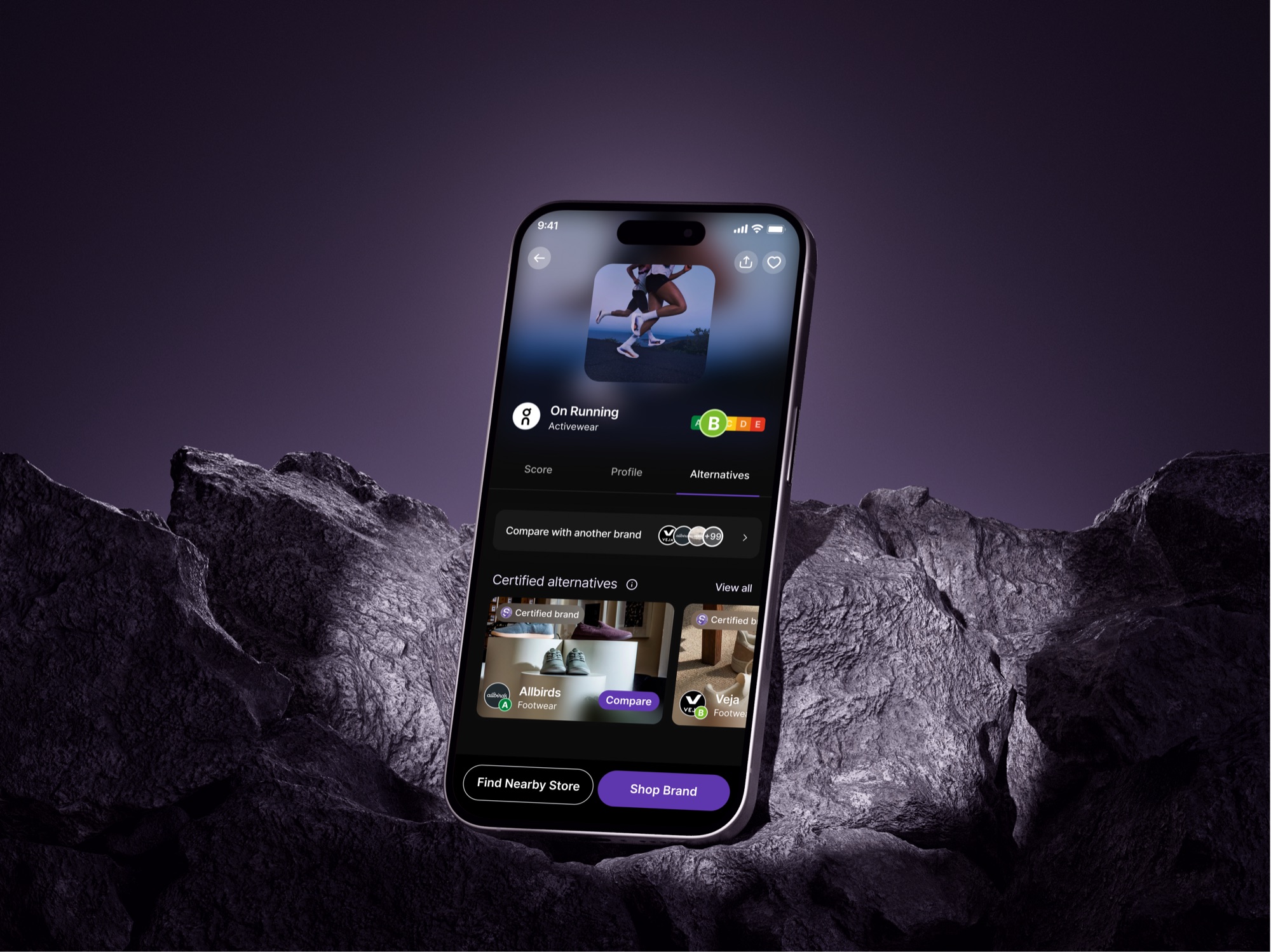 Scored app screen comparing a brand against certified alternatives, phone mockup on rock